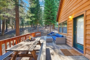 Eine Holzterrasse mit Gartenmöbeln, einem Picknicktisch und Blick auf einen Wald.