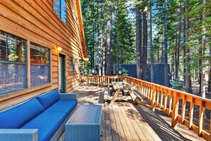 Eine Holzterrasse mit einer Couch und einem Tisch, umgeben von einem Wald.