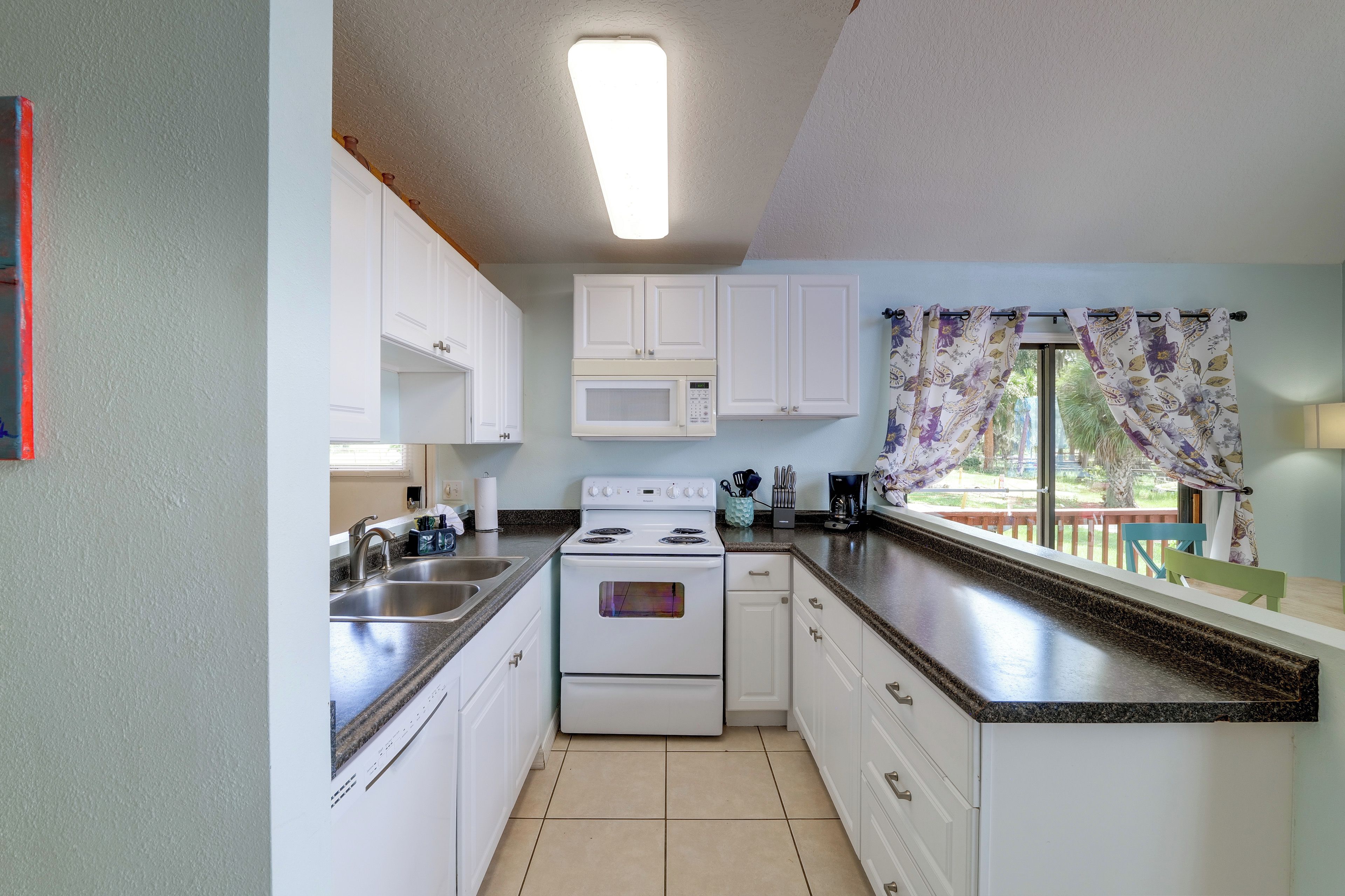 A kitchen with white cabinets, a stove, a microwave, and a window with curtains.