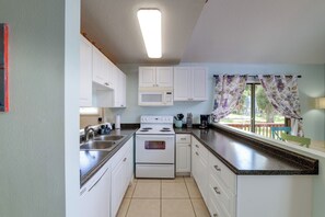 A kitchen with white cabinets, a stove, a microwave, and a window with curtains.