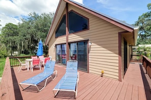 A two-story building with a deck, outdoor seating, and a large window.