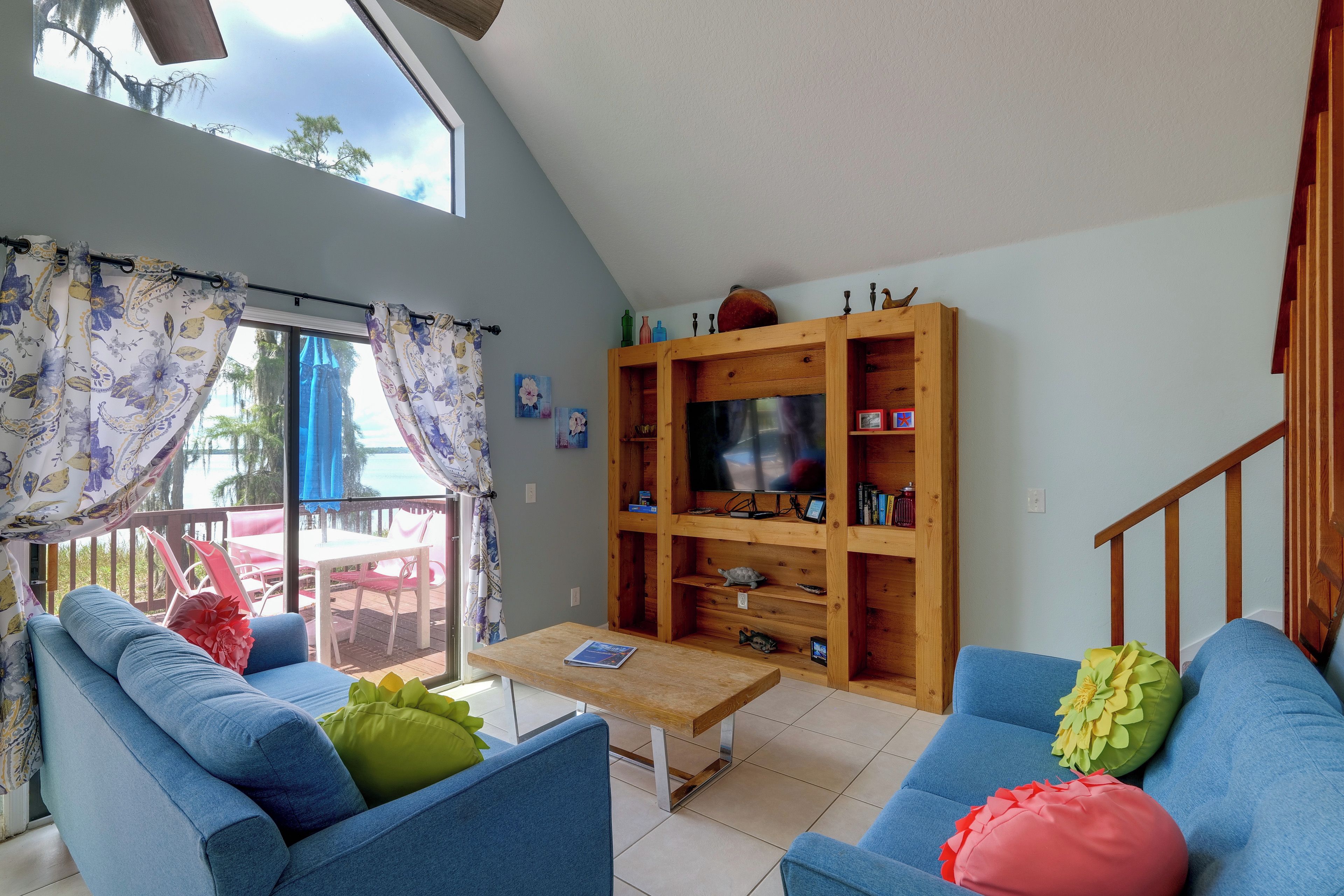 Un salon avec un canapé bleu, un meuble TV en bois et une vue sur l’extérieur.