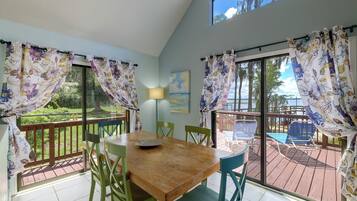 Un coin repas avec une table en bois, des chaises vertes et une vue sur une terrasse et sur du mobilier d’extérieur.