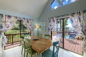 A dining area with a wooden table, green chairs, and a view of a deck and outdoor furniture.