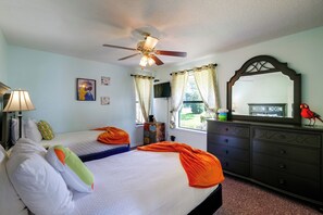 A bedroom with a bed, a dresser, a ceiling fan, and a window with curtains.
