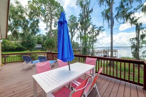 A deck with a table and chairs, overlooking a body of water and surrounded by trees.