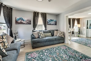 Ein Wohnzimmer mit grauem Sofa, passendem Sessel und floralen Teppichen.