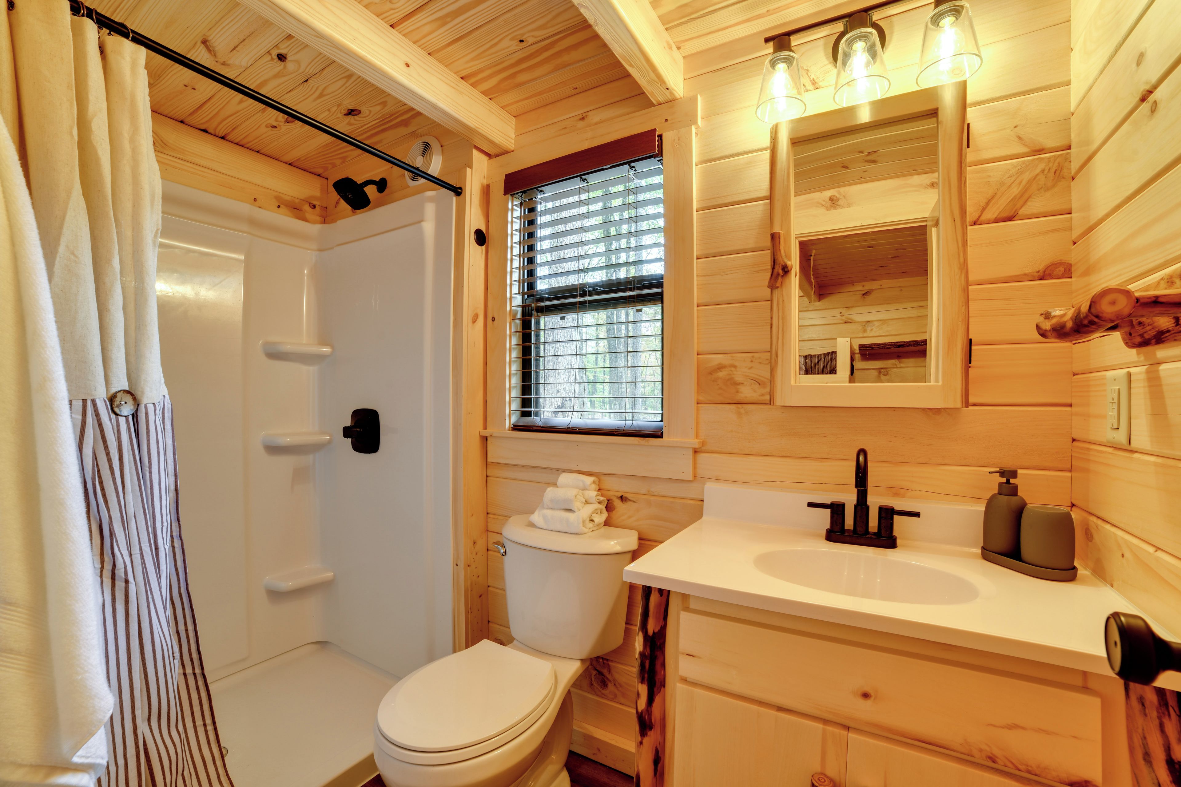 Une salle de bain rustique, aménagée dans une cabane en bois, avec douche, toilettes et lavabo.