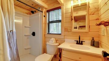 Une salle de bain rustique, aménagée dans une cabane en bois, avec douche, toilettes et lavabo.