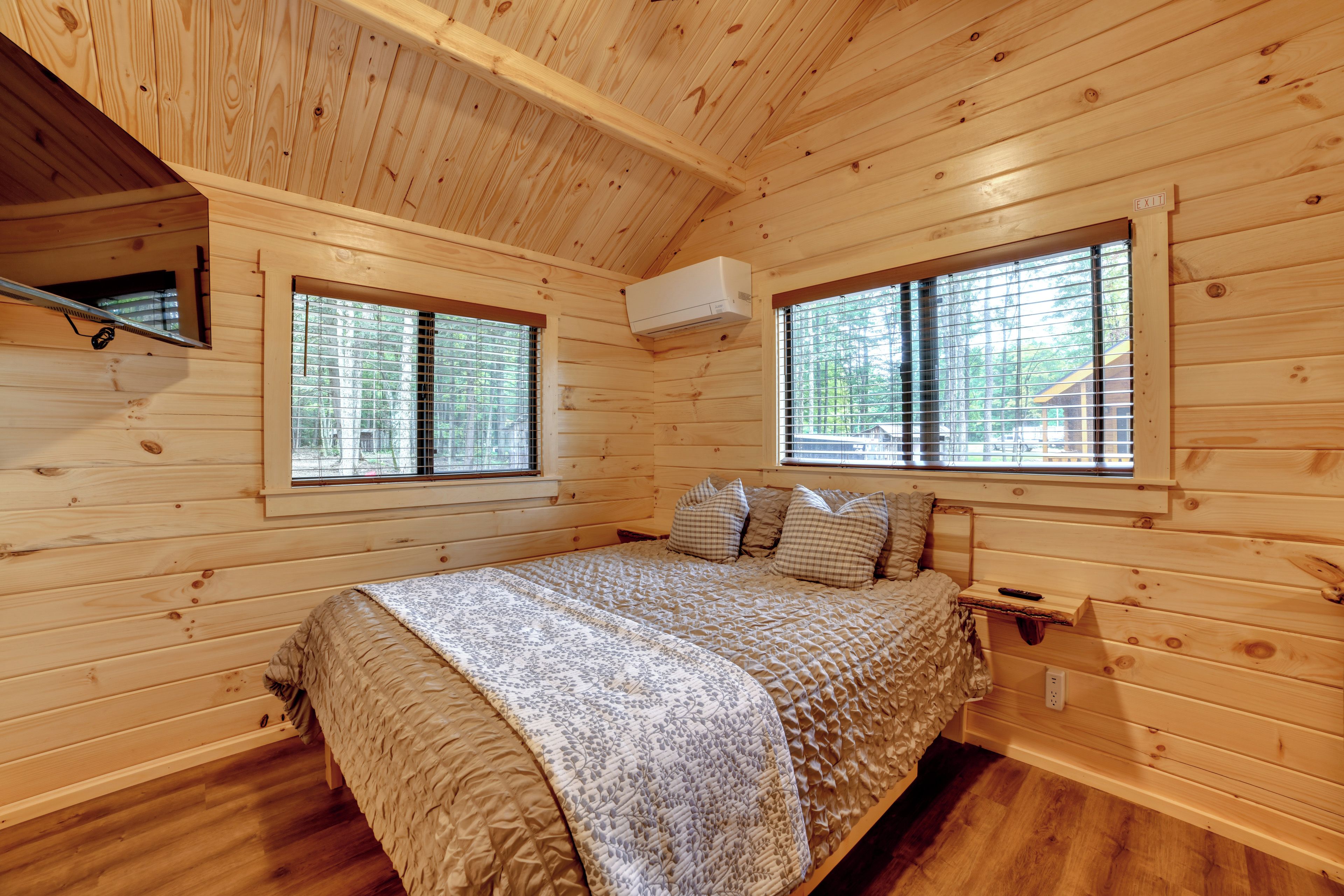 Une chambre dans une cabane en bois, avec un lit, deux fenêtres et un appareil de climatisation.