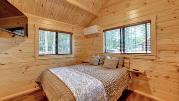 Une chambre dans une cabane en bois, avec un lit, deux fenêtres et un appareil de climatisation.