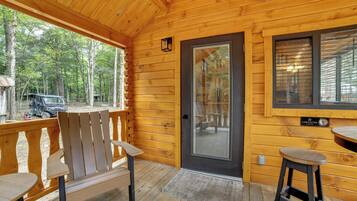 Une cabane en bois avec une véranda, deux chaises, une table et une porte dotée d’une fenêtre.