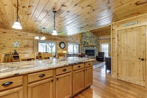 A spacious kitchen with wooden cabinets, a large island, and a stone fireplace. - 5 Mi to Cataloochee Ski! Mtn-View Retreat w/ Deck (Maggie Valley)