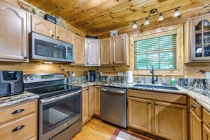 A kitchen with wooden cabinets, stainless steel appliances, a granite countertop, and a window with blinds. - 5 Mi to Cataloochee Ski! Mtn-View Retreat w/ Deck (Maggie Valley)