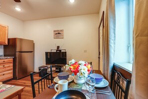A compact kitchen with a refrigerator, a dining table set with plates, a vase of flowers, and a flat-screen TV. - Cozy Apartment Near UAF & Downtown Fairbanks! (Fairbanks)