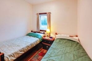 A small, single-room accommodation with two single beds, a nightstand with a lamp, and a window with curtains. - Cozy Apartment Near UAF & Downtown Fairbanks! (Fairbanks)