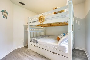 Ein Etagenbett mit dekorativem Rad und Kuscheltieren, eine weiße Wand mit Wandbild sowie ein Holzboden.