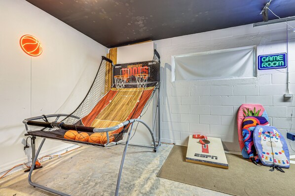 Ein Basketballkorb mit Netz, eine Wand mit einer Neonreklame und eine Tür mit der Aufschrift 'GAME ROOM'.