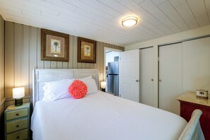 Ein Schlafzimmer mit einem Bett, einem Nachttisch, einer Kommode, einer Tür und einer Wand mit zwei gerahmten Bildern.