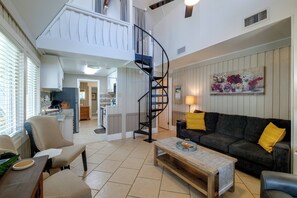 A spacious living area with a curved staircase, a sofa with yellow cushions, and a coffee table. - Lake Breeze Bungalow: 3 Mi to State Park! (Clermont)