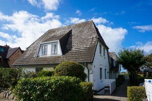 A two-story house with a sloped roof, a visible attic window, and a front porch. - Kapitänskoje - Comfortable Apartment in Keitum with a Beach Chair on the Beach at (Sylt)