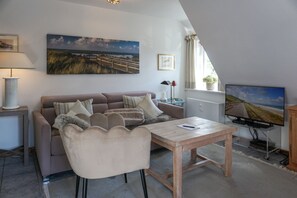 A cozy living room with a sofa, a coffee table, and a television. - Kapitänskoje - Comfortable Apartment in Keitum with a Beach Chair on the Beach at (Sylt)