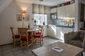 A cozy kitchen with a dining area, featuring a wooden table, chairs, and a kitchen counter with appliances. - Kapitänskoje - Comfortable Apartment in Keitum with a Beach Chair on the Beach at (Sylt)
