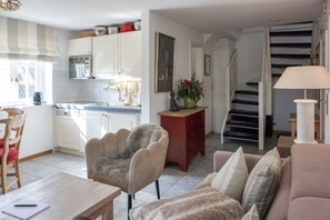 A living room with a sofa, a chair, a table, a staircase, and a kitchen area with cabinets and a sink. - Kapitänskoje - Comfortable Apartment in Keitum with a Beach Chair on the Beach at (Sylt)