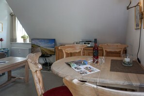 A dining area with a round table, chairs, a bottle of wine, glasses, and a candle. - Kapitänskoje - Comfortable Apartment in Keitum with a Beach Chair on the Beach at (Sylt)
