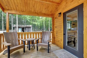 Une terrasse en bois avec des fauteuils Adirondack et une table, donnant sur une zone boisée.