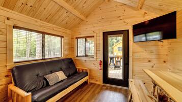 L’intérieur d’un chalet en bois, avec un canapé en cuir, des murs en bois et un téléviseur fixé au mur.