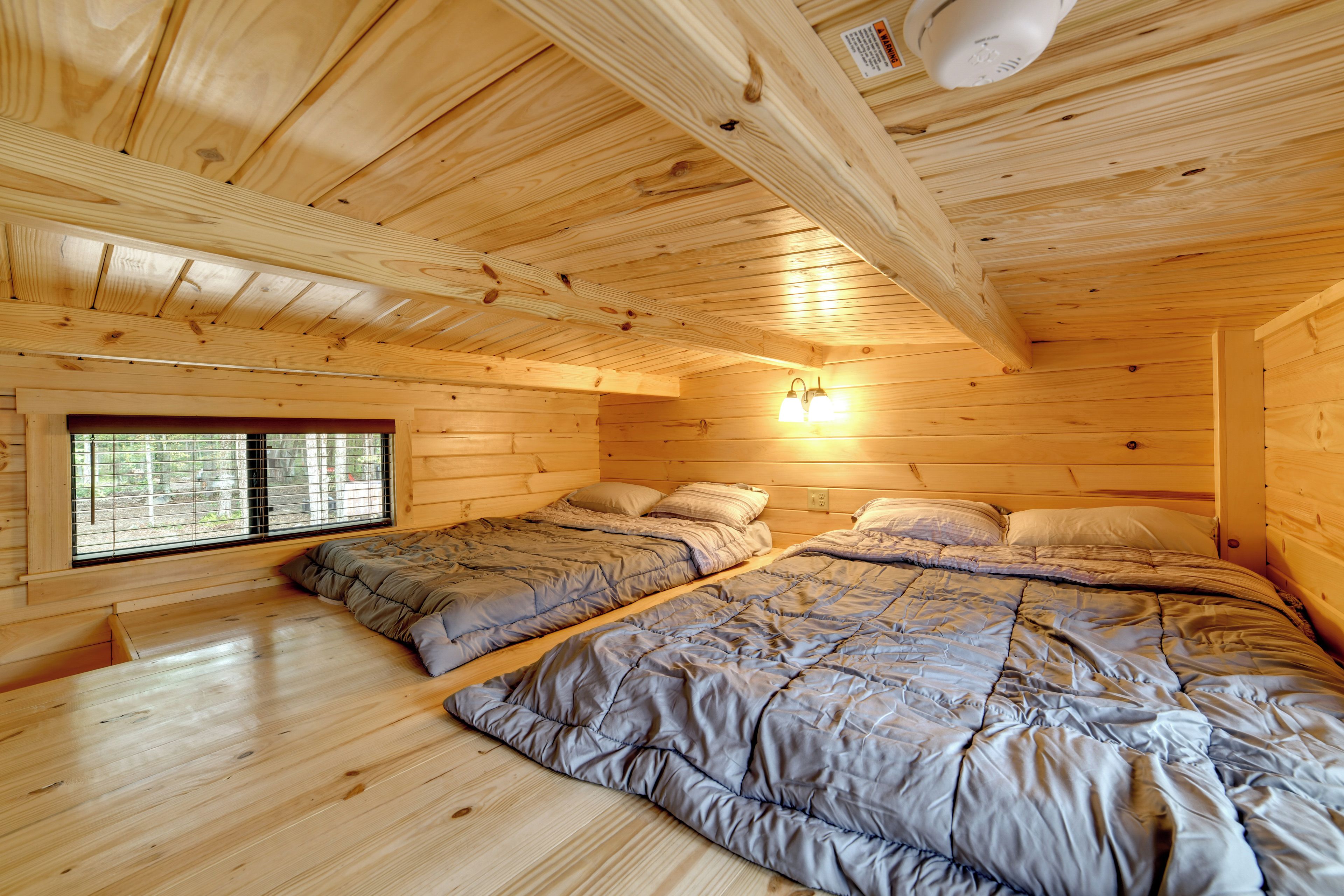 Une chambre de cabane en bois avec deux lits, une fenêtre et un luminaire au plafond.
