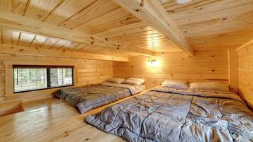 Une chambre de cabane en bois avec deux lits, une fenêtre et un luminaire au plafond.