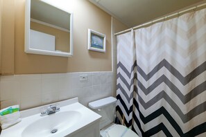 Un bany amb un lavabo blanc, un vàter, un mirall i una cortina de bany amb dibuix de zigzag.