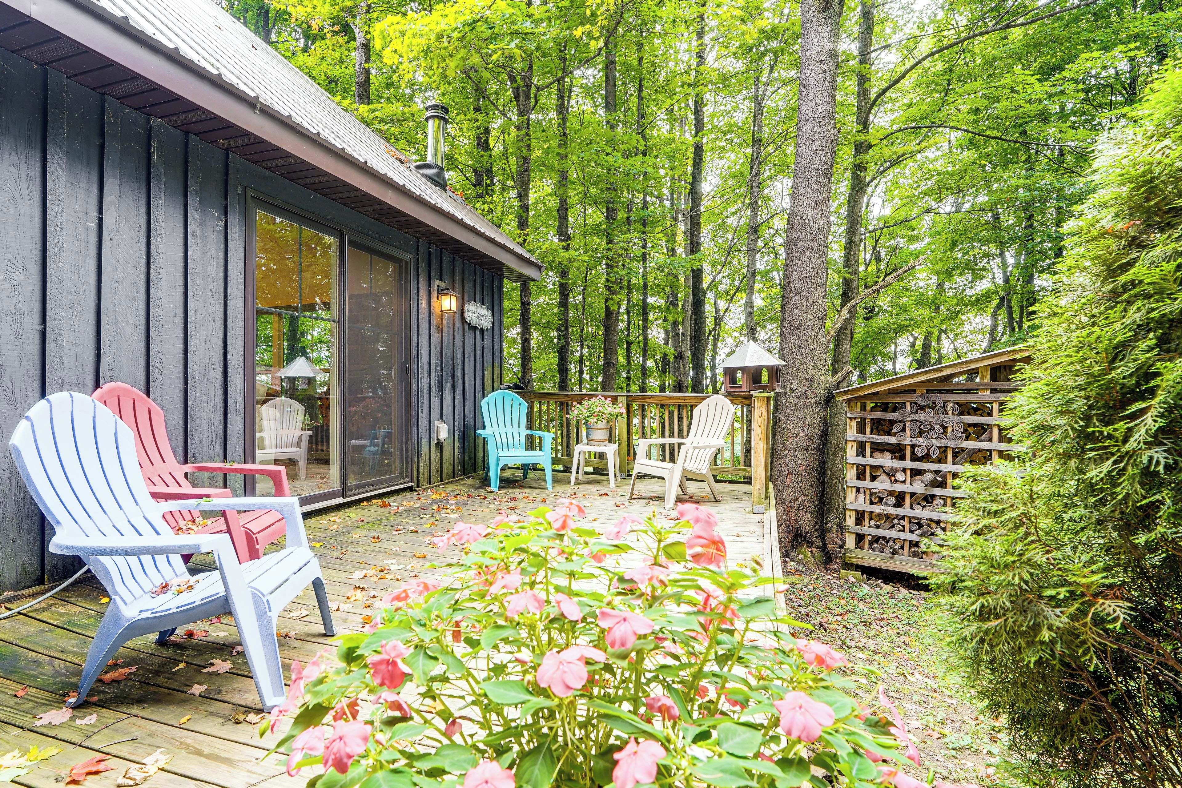 A wooden deck with Adirondack chairs, a glass door entrance, and a wooden fence with a stack of firewood.