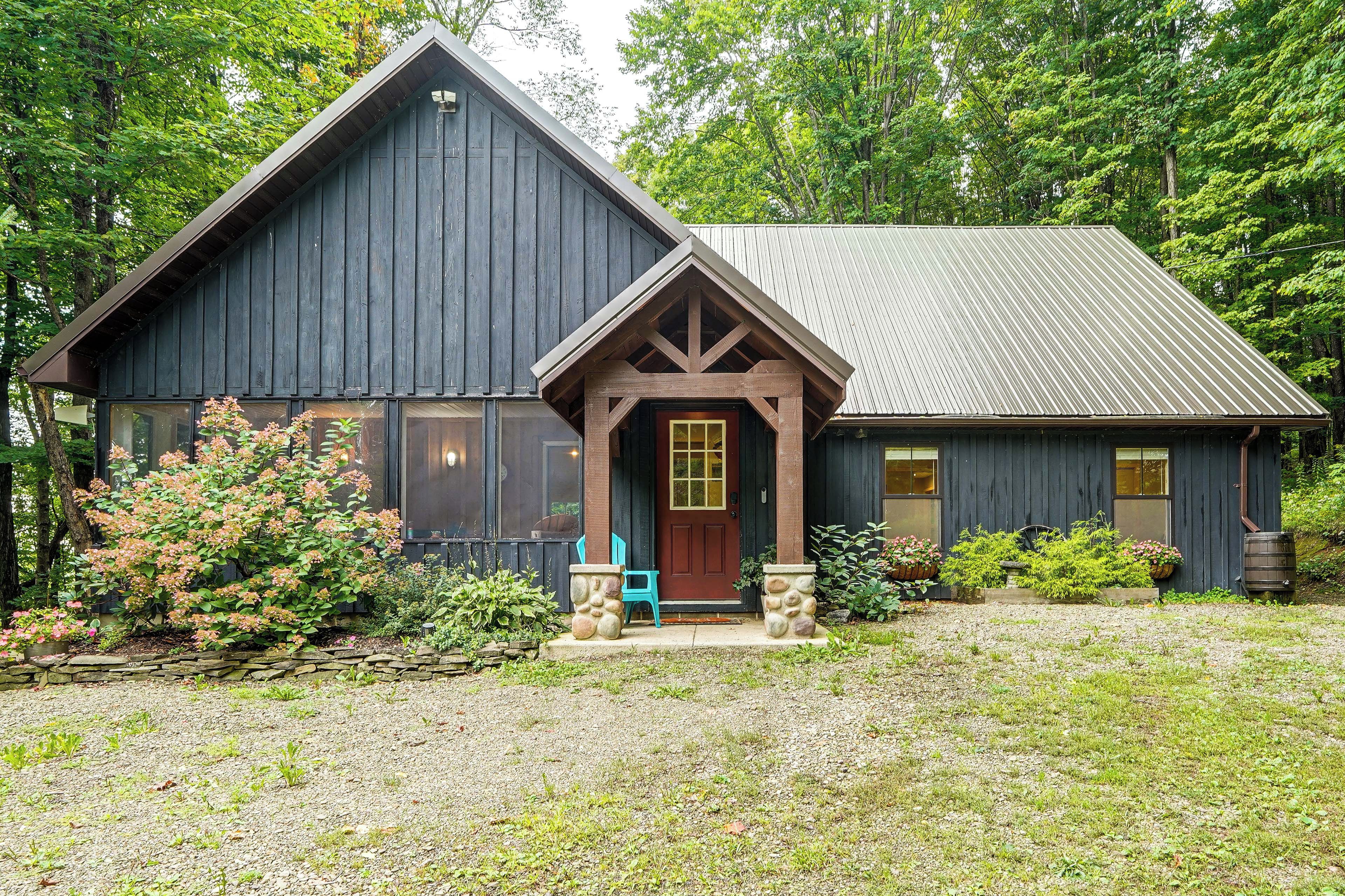 A rustic cabin with a prominent front porch, large windows, and a metal roof.