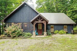 Une cabane rustique dotée d’une véranda bien visible à l’avant, de grandes fenêtres et d’un toit en métal.