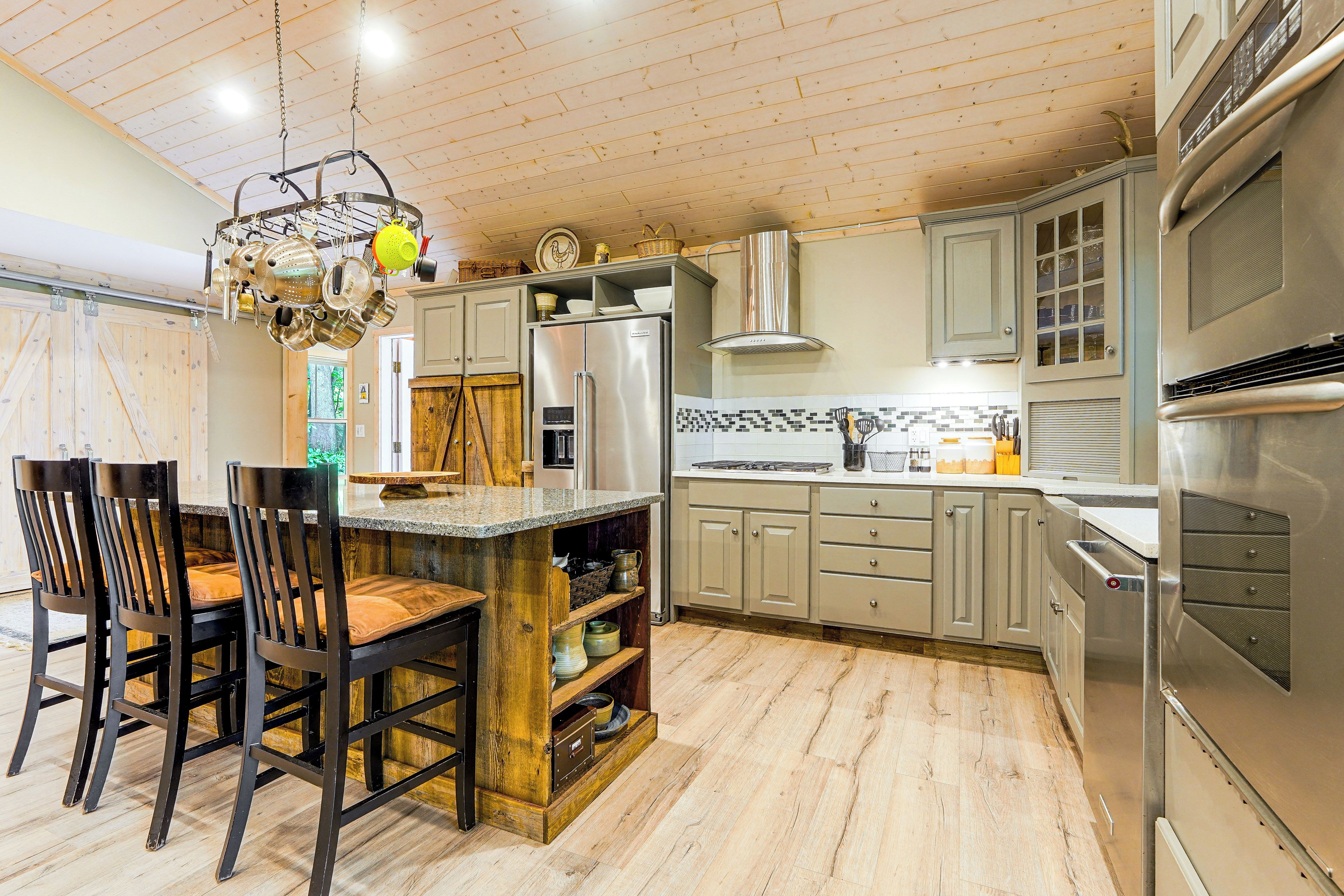 A kitchen with a central island, wooden chairs, a stainless steel refrigerator, and a built-in oven.