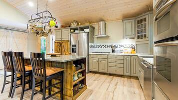 A kitchen with a central island, wooden chairs, a stainless steel refrigerator, and a built-in oven.