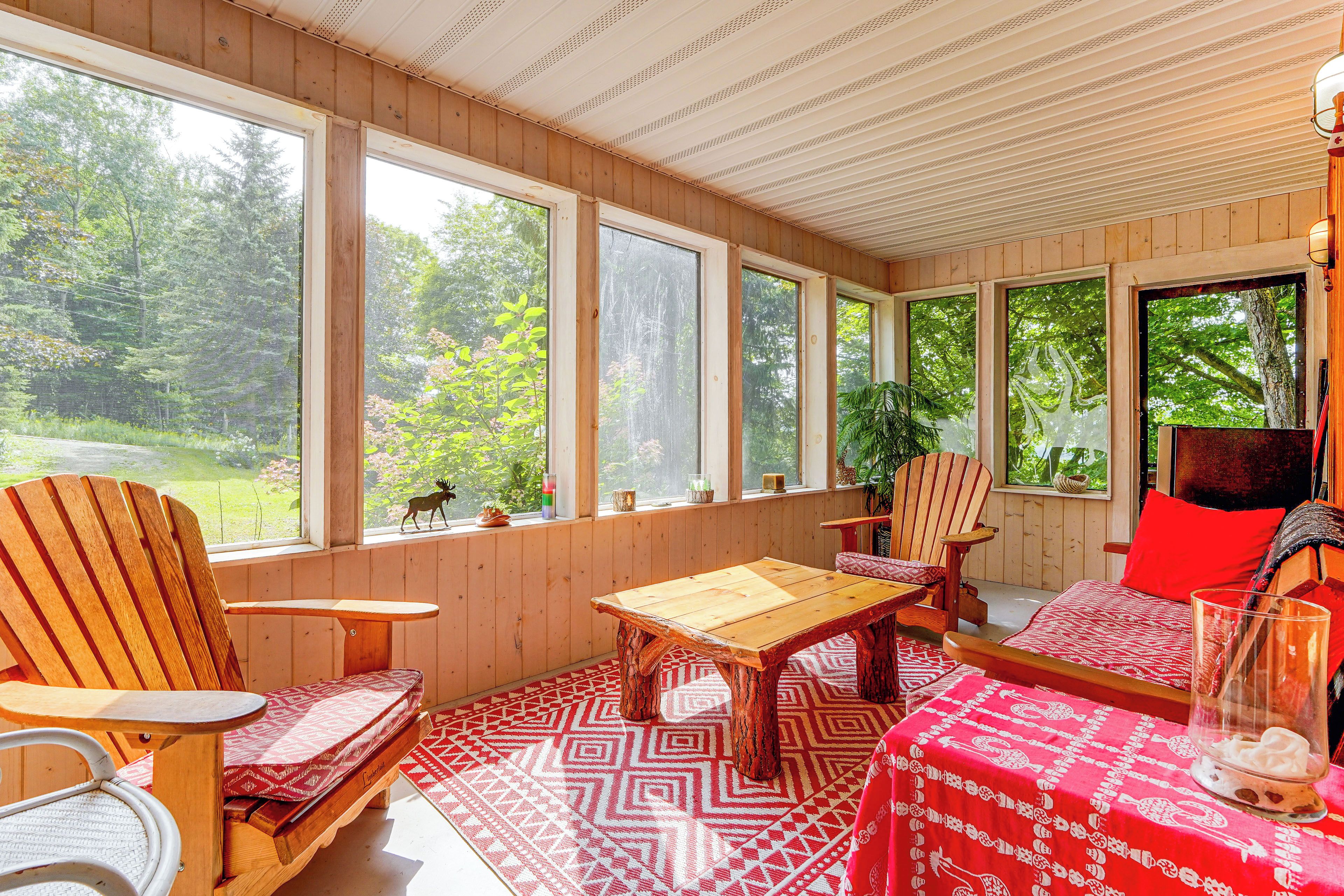 A room with wooden walls and large windows, a wooden table, two chairs, a sofa, and a patterned rug.