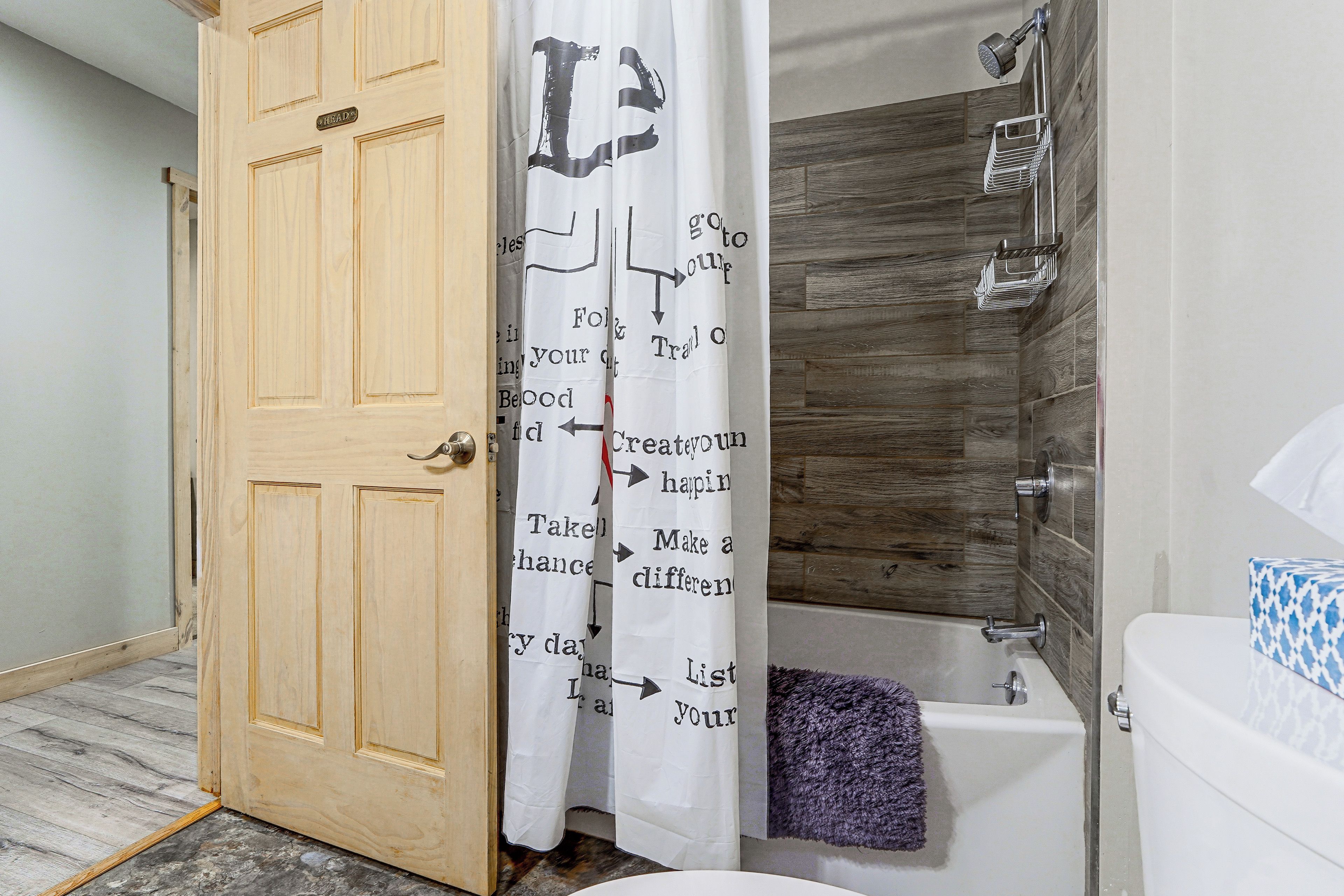 Une salle de bain avec une porte en bois, une douche à pommeau large et une baignoire.