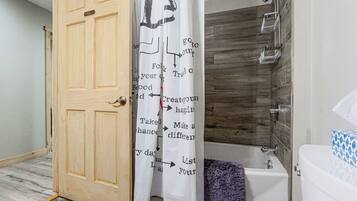 Une salle de bain avec une porte en bois, une douche à pommeau large et une baignoire.