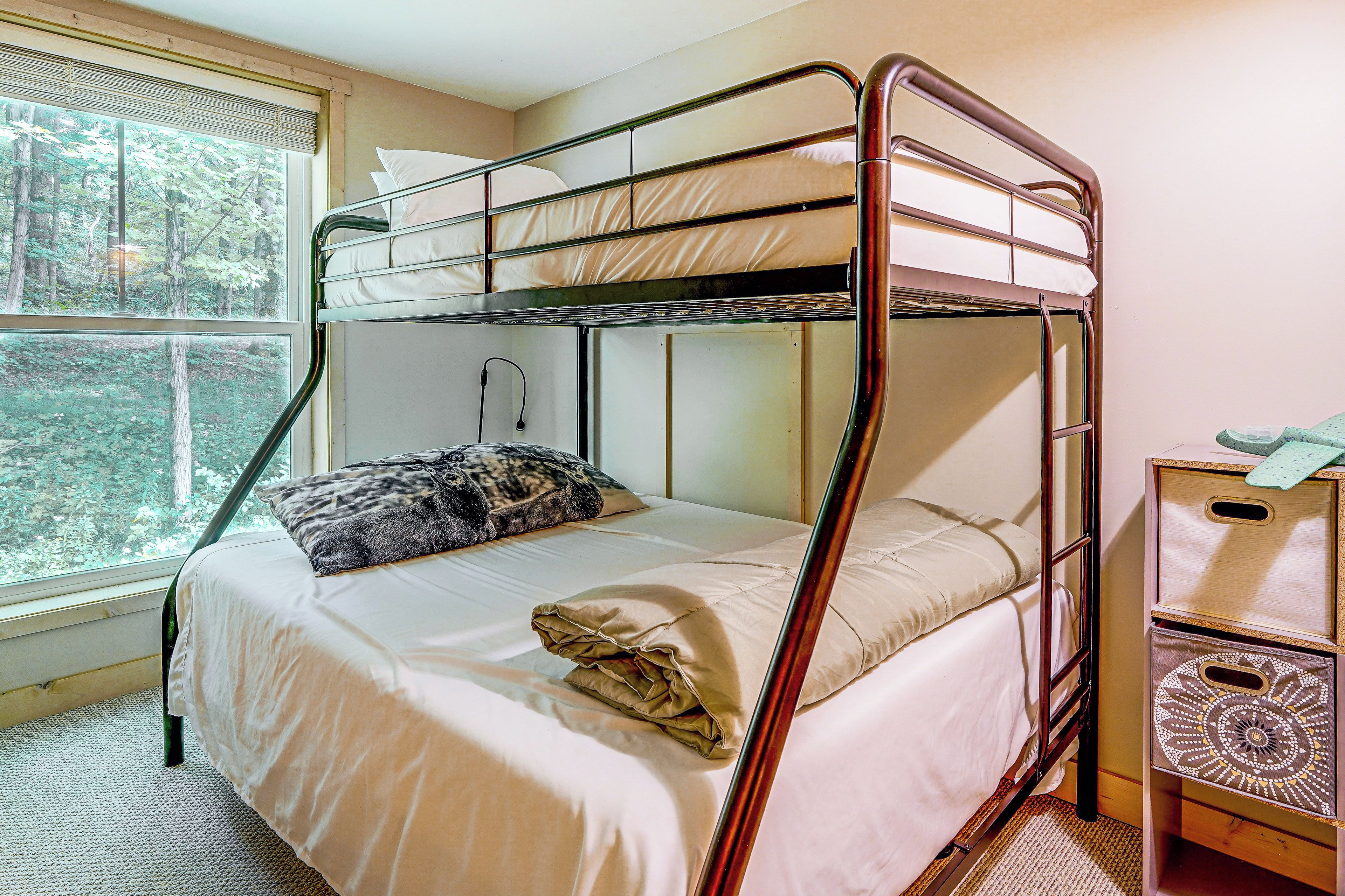 A bunk bed with a window view, a bedside table, and a patterned rug.