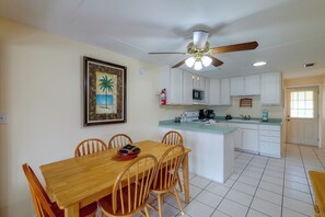 Une cuisine avec des meubles blancs, une table à manger en bois et un ventilateur de plafond.