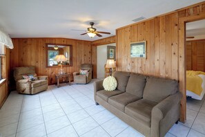 Ein Zimmer mit Holzvertäfelung, einem Deckenventilator, einem Sofa, zwei Sesseln, einem Tisch und einer Lampe.