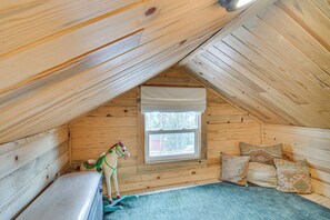 A wooden attic bedroom with a sloped ceiling, a window, a bed, and a decorative toy horse. - Historic Wondervu Cabin Near Gross Reservoir (Golden)