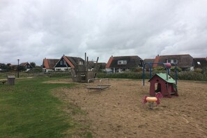 Ein Spielplatz mit Schaukel, Rutsche und einer kleinen Spielhaus-Konstruktion.