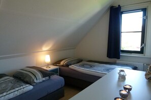 Ein kleiner, gemütlicher Raum mit zwei Betten, einem Tisch mit Kerzen und einem Fenster mit Vorhängen.