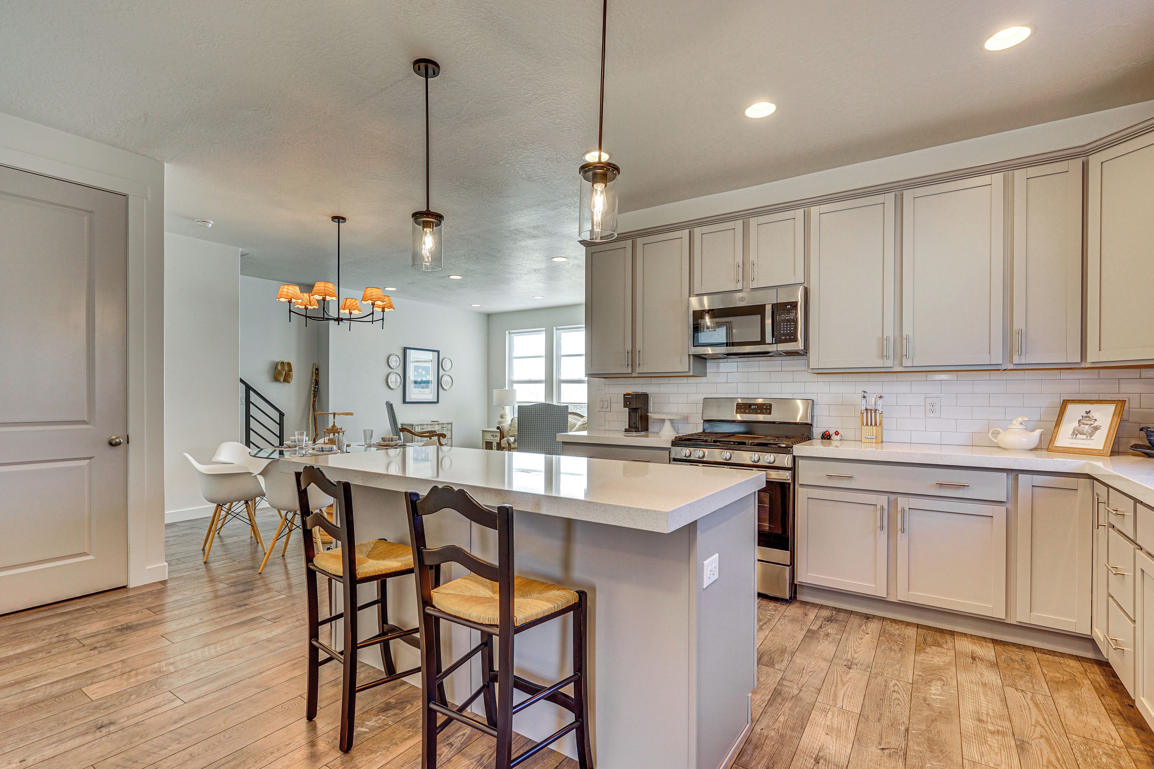 A modern kitchen with a central island, bar stools, stainless steel appliances, and pendant lighting.