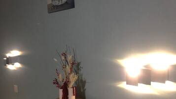 A room with a wooden table, a vase with dried flowers, and wall-mounted lights.
